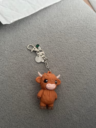 Reviewer's brown plastic Highland Cow keychain with a silver-colored clasp on a grey surface.