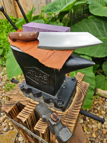 Customer's cleaver-style knife with a satin finish, achieved using the sanding belts, resting on an anvil.