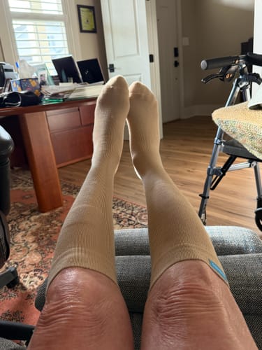 A reviewer wearing knee-high tan Performance Eucalyptus Compression Socks with their legs propped up indoors.