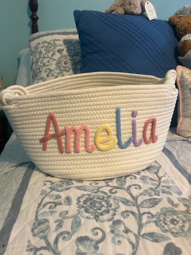 Customer's white knitted basket personalized with the name Amelia in pastel-colored yarn.