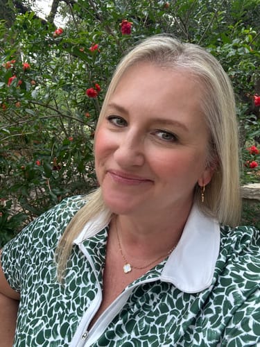 Reviewer smiling outdoors, wearing a gold clover pendant necklace and a small hoop earring from the Spring Box.