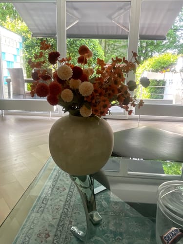 Klant toont de beige Terra vaas, gevuld met een groot boeket herfstbloemen in de woonkamer.