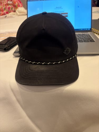 Customer's black Big Flat Bill Rope Sport Hat showing some visible wear on a table.