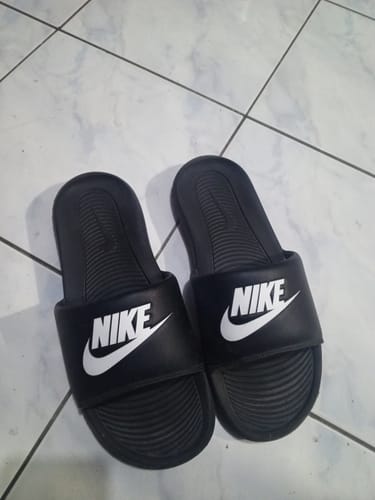 Customer's pair of black Nike Men's Victori One Slides with the white logo, shown on a tiled floor.