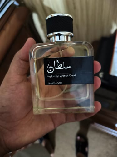 A customer holding the clear, square bottle of Sultan perfume, showing its black label with white text.