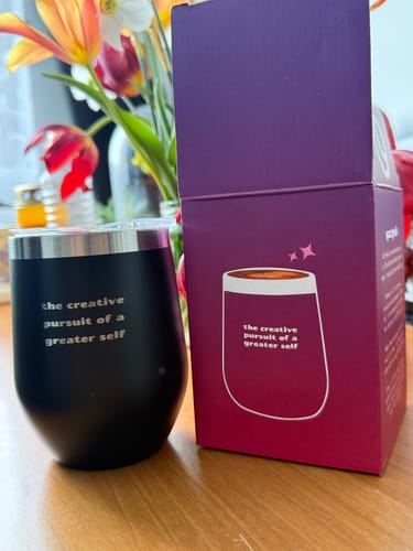 Customer's black insulated cup with white text, placed on a table next to its purple packaging.