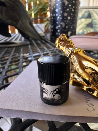 Close-up of a customer's small Sinister perfume bottle with its spooky label on a patio table.