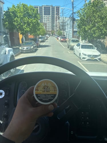 Reviewer holding a can of Drifters Island Peach Nicotine Pouches in the driver's seat of a vehicle.