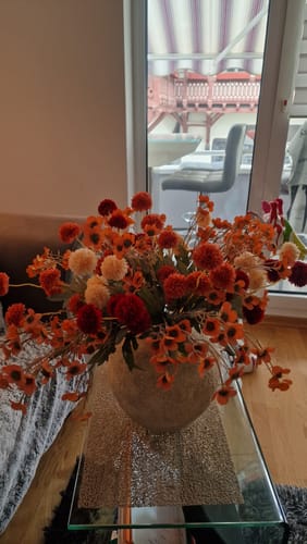 Recensent toont de beige Arda vaas op een glazen tafel, gevuld met kleurrijke kunstbloemen.