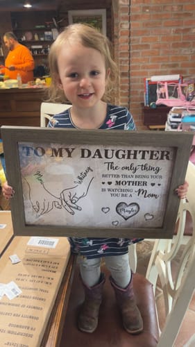 A smiling young girl holding the customer's framed 'To My Daughter' personalized poster.