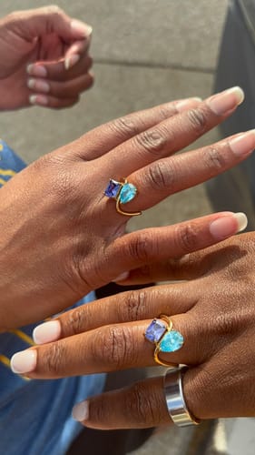 Customers' hands showing two matching Navae Birthstone Rings with purple and light blue stones.