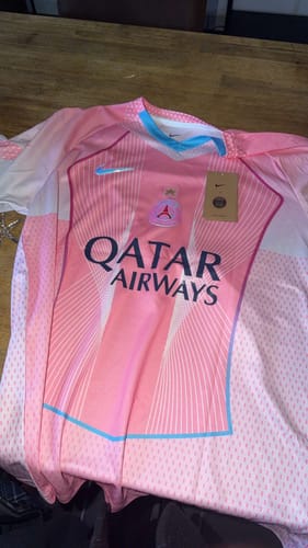 Client montrant le devant du maillot concept PSG 25/26 rose posé sur une table.