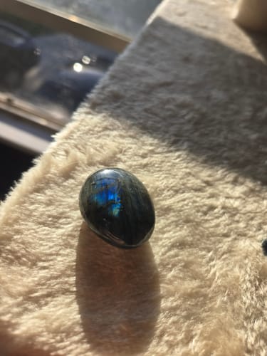 Customer's labradorite palm stone from the VIP Crystal Club resting on a fuzzy surface, with a blue iridescent flash.