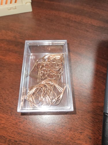 Reviewer's Rose Gold Heart Shaped Paper Clips inside their clear storage box on a wooden desk.