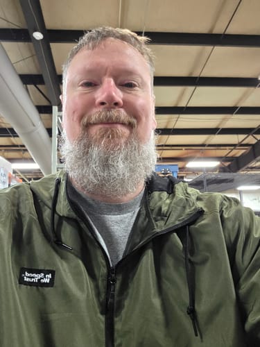 Customer wearing the olive Anorak jacket with a grey shirt underneath in an indoor setting.