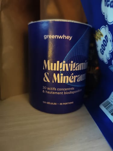 Un client montre le pot bleu des Multivitamines & Minéraux sur une surface.