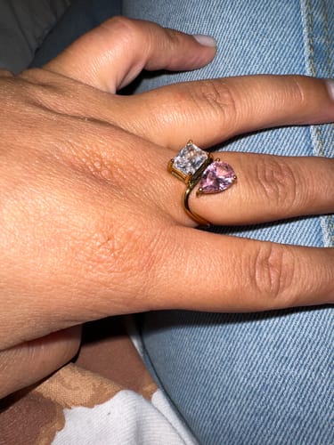 Customer's hand wearing the gold Navae Birthstone Ring with one clear and one pink stone.