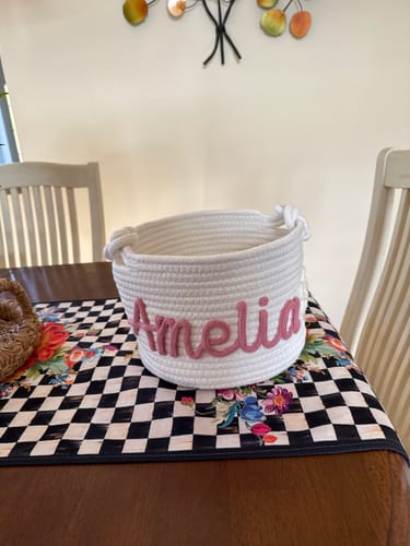 Customer's personalized white rope basket with 'Amelia' in pink lettering, set on a table.