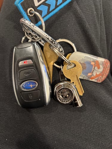Customer's Turbo Keychain on a key ring with a car fob and several other keys against a dark shirt.