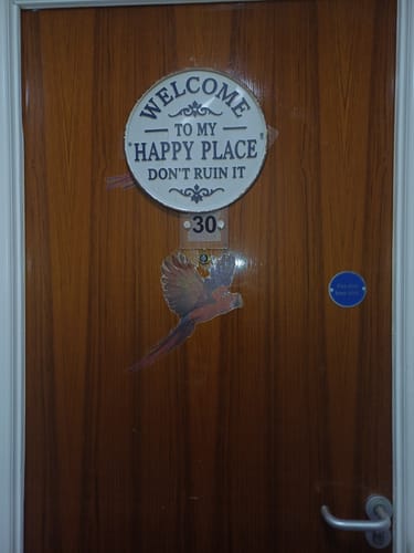 Customer's round metal 'Welcome To My Happy Place' sign hanging on a brown wooden door.