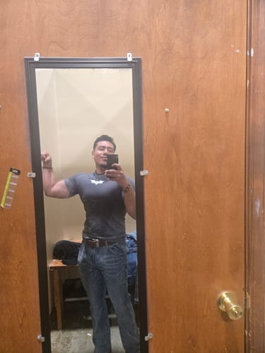 Reviewer in a fitting room taking a mirror selfie while flexing in a grey Batman Compression Tee.