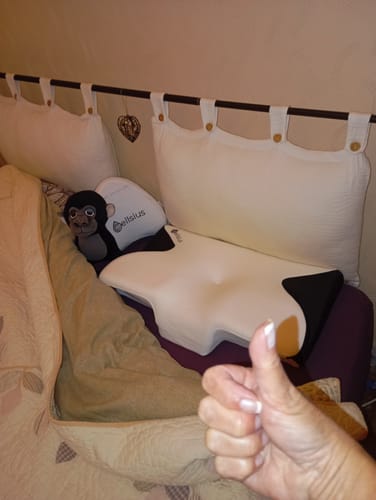 Cliente satisfaite montrant son Oreiller Papillon Cervical Cellsius sur un lit avec un pouce levé.