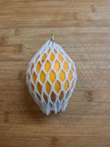 Rezensent zeigt eine Süße Granadilla im weißen Schutznetz auf einem Holzbrett.