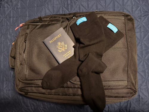 Reviewer's black compression socks laid out on a travel bag next to a passport.