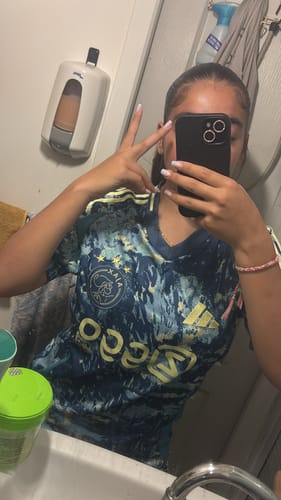 Une cliente prend un selfie dans un miroir en portant le maillot extérieur bleu de l'Ajax Amsterdam.