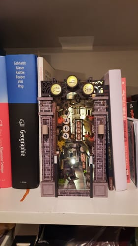 Customer's assembled Old Shanghai Book Nook Kit glowing brightly on a bookshelf between two books.