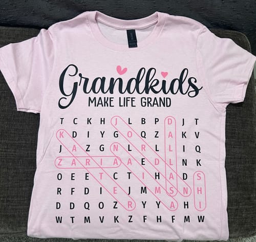Customer's pink personalized shirt with a 'Grandkids make life grand' word search puzzle.