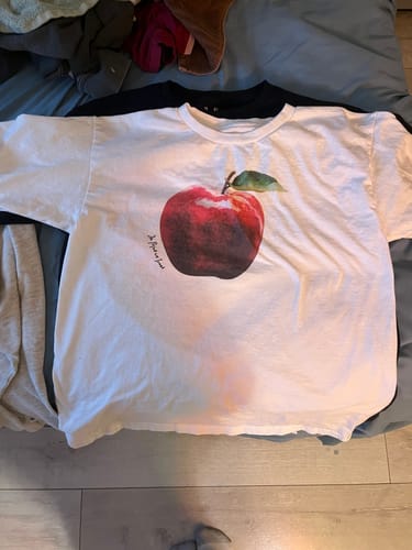 Customer's white rotten baby tee with a large apple graphic laid out flat.