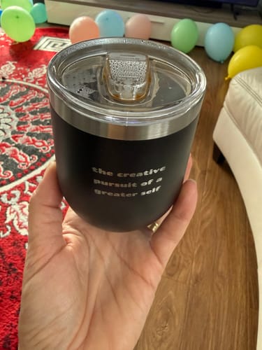 Reviewer's hand holding the black insulated cup with its clear, splash-proof lid on.