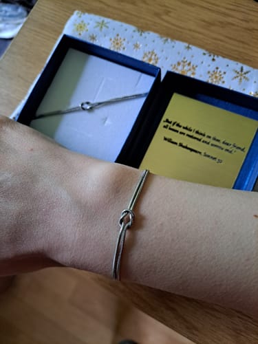 Reviewer showing the silver-colored Forever Knot Bracelet on their wrist, with the open product box in the background.