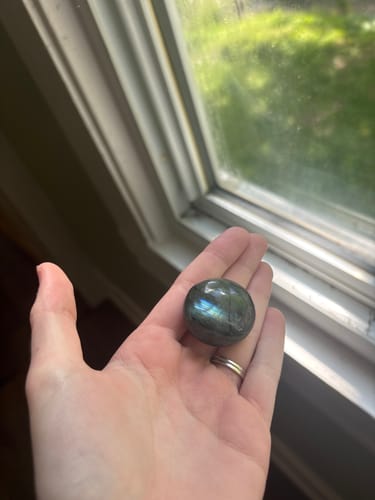 Customer holding a round, shimmering crystal in their hand by a window.