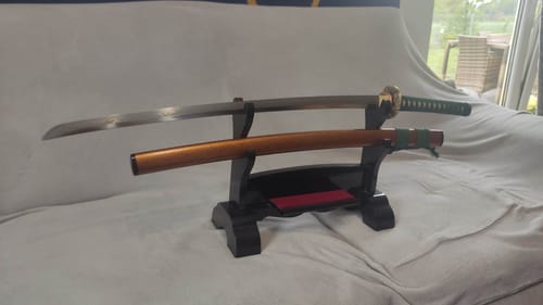 Reviewer's Katana - Verdant Wave displayed on a stand, unsheathed to show the shiny blade and orange scabbard.