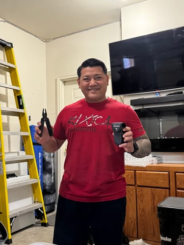Reviewer smiling while holding the Multi-Tool Pliers and its black carrying pouch indoors.