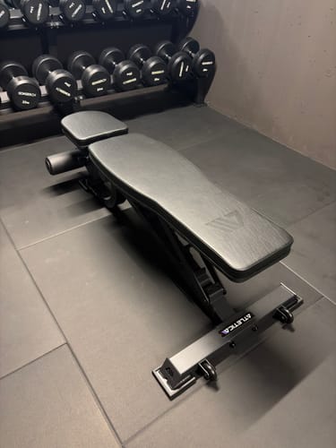 Ein Rezensent zeigt die aufgebaute, schwarze B2 Situp Hantelbank in einem Fitnessraum.