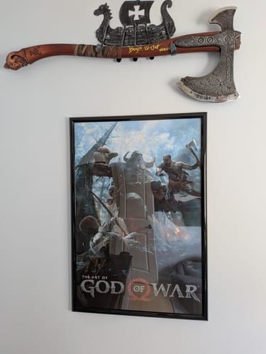 Reviewer's signed Ragnarok Kratos axe mounted on a decorative Drakkar wall holder above a poster.