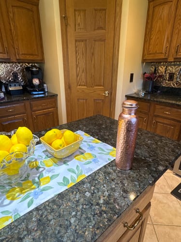 Customer's hand-hammered copper water bottle standing on a kitchen island next to bowls of lemons.