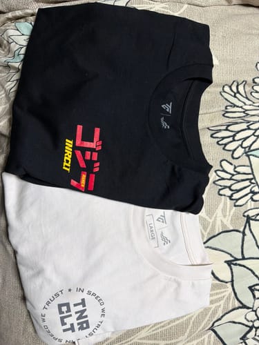 Customer's black VOLCANIC WAVES TEE folded next to a white t-shirt on a patterned surface.
