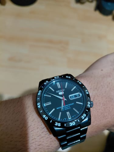Un cliente muestra el reloj Seiko 5 negro en su muñeca en una habitación iluminada.