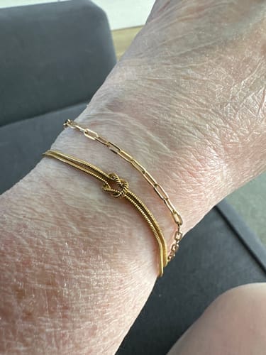 Reviewer's wrist showing the gold Forever Knot Bracelet worn with another thin chain bracelet.
