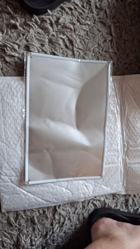 Customer's funny wall art tin sign shown crumpled and dented, resting on its thin packaging on a carpet.