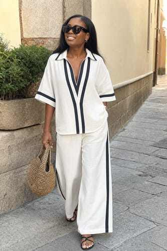 Reviewer walking outdoors in the white wide-leg pants with black contrast stripes as part of a matching set.