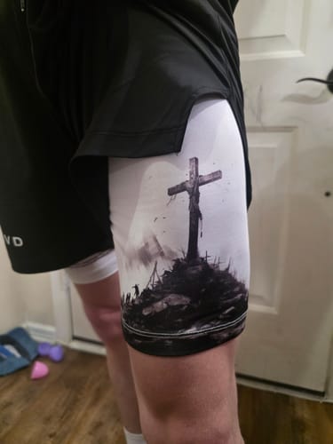 Close-up of a reviewer wearing the Soldier's Faith Performance Shorts, showing the black crucifixion graphic on the white inner layer.