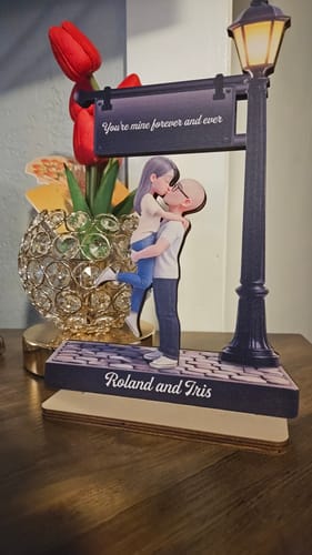 Customer's personalized wooden plaque of a couple kissing under a lamppost, displayed on a wooden table.