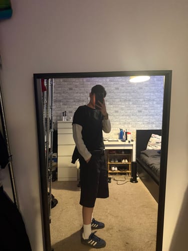 Reviewer showing the fit of the black blank baby tee layered over a long-sleeve shirt in a mirror selfie.