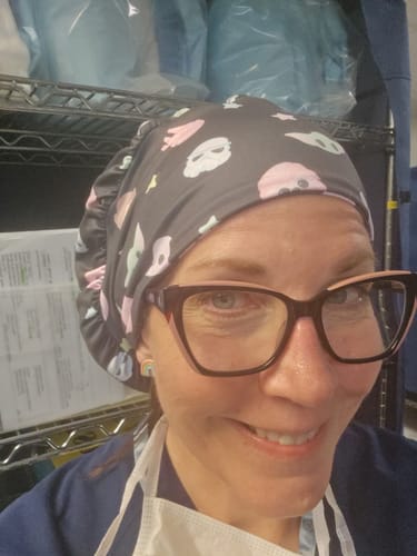 Close-up of a reviewer smiling while wearing the patterned 'May The Fourth' DuoStyle Scrub Hat in a medical setting.