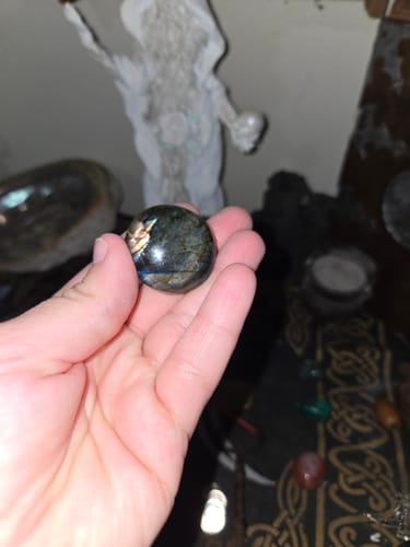Customer's hand holding a polished round labradorite crystal, showing its iridescent flashes of color.